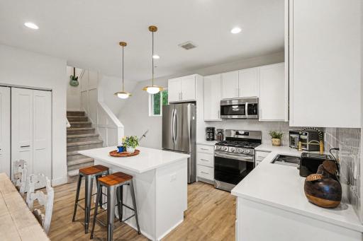 Kitchen boasts gold hardware, gold faucet, SS appliances and an island with seating. The convenient pantry is left of the stairs.