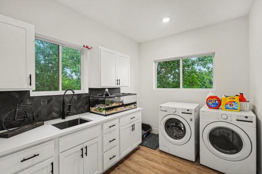 The upper level laundry room is impressive with windows on 2 sides, built in cabinets with black hardware and a large sink with a black faucet.