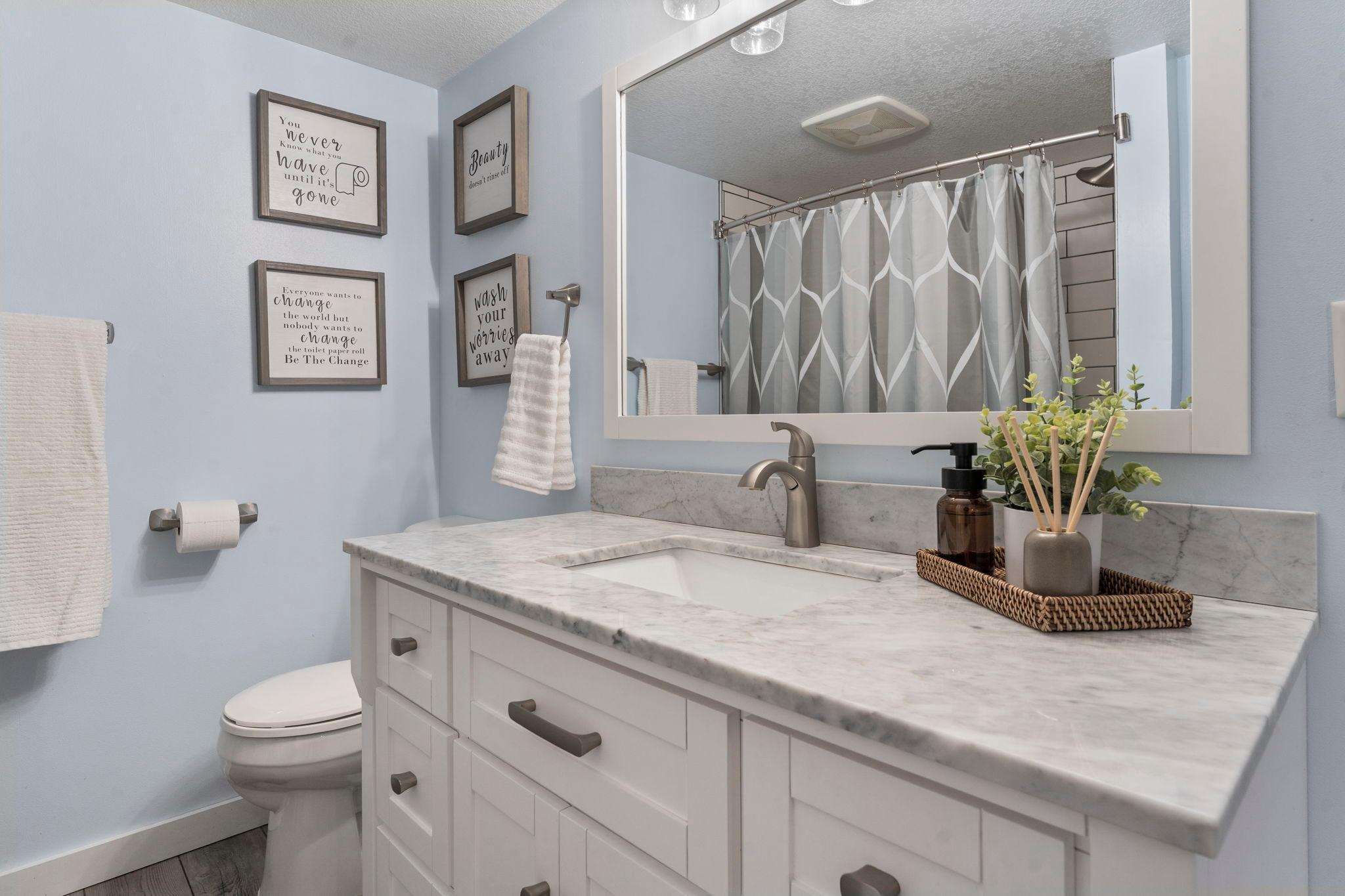 Nearby is a beautifully updated full bathroom with a single vanity, luxury plank flooring, and a tub/shower combination.