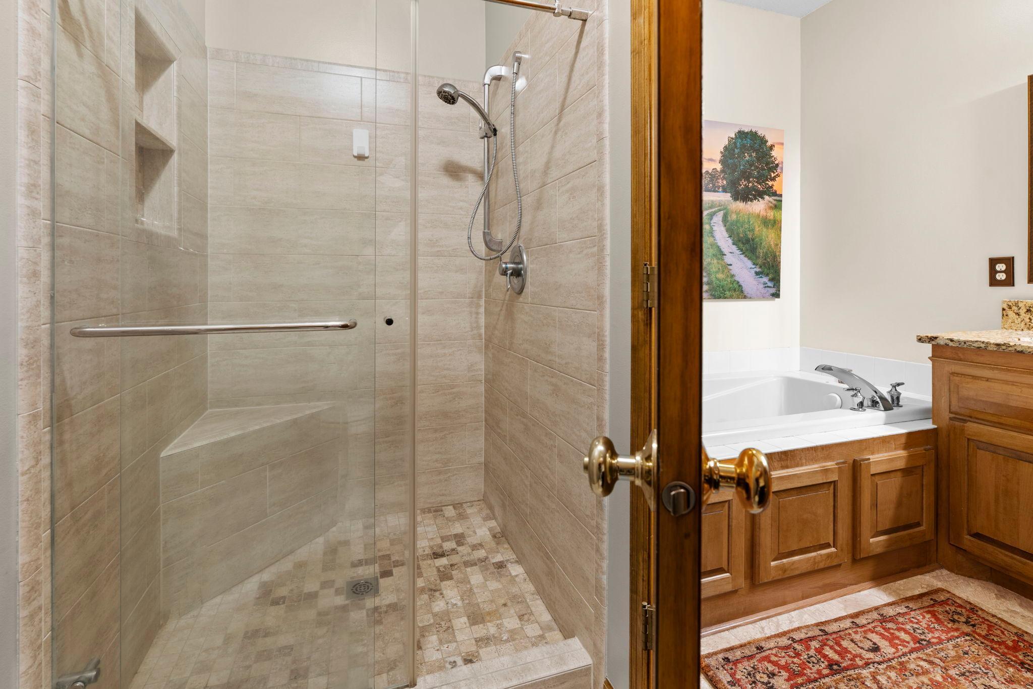 The full ensuite bathroom is complete with a double vanity, tile flooring, a soaking tub, and a walk-in tiled shower.