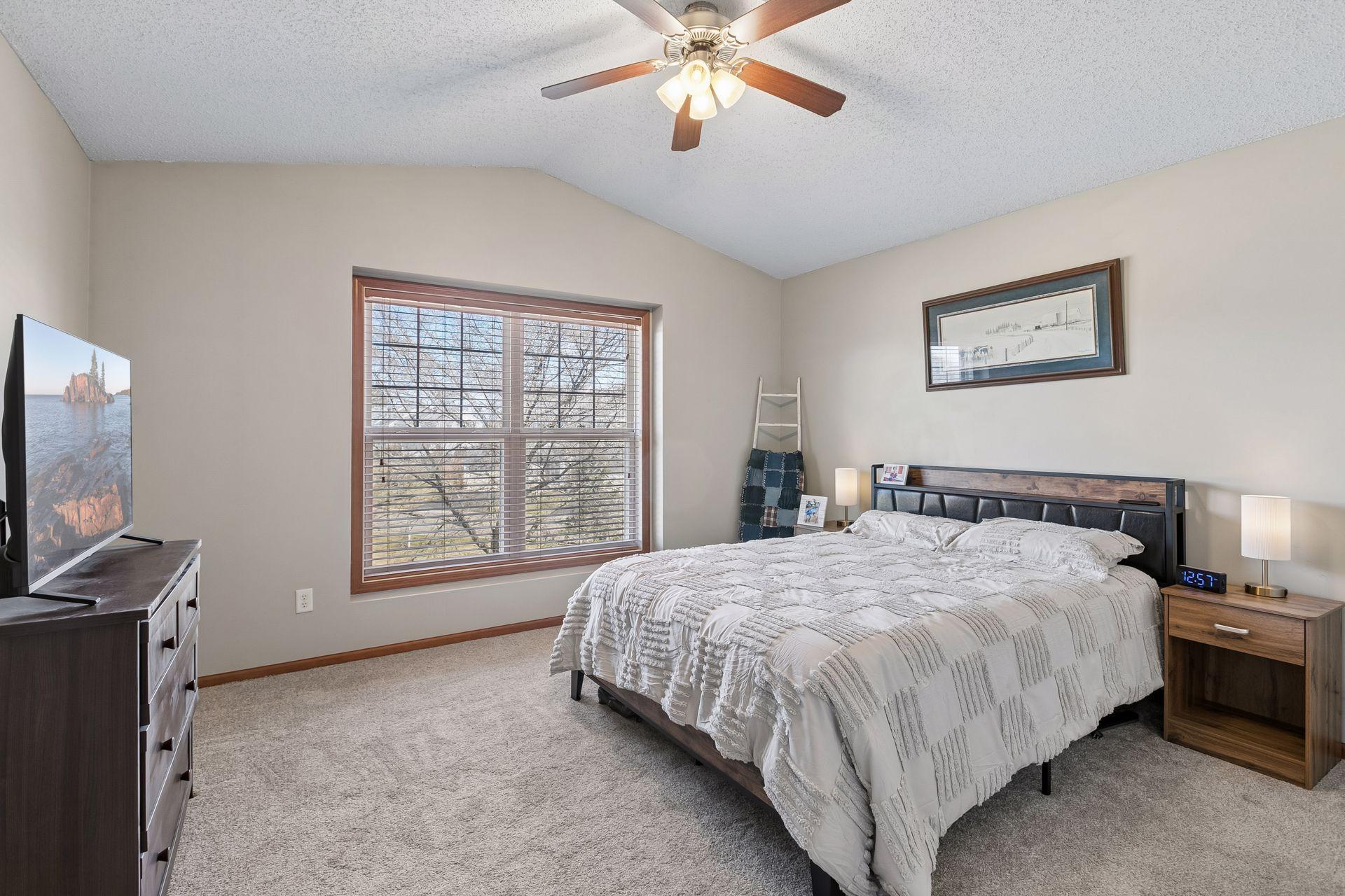 Upper level primary suite with vaulted ceiling, large window and ceiling fan.