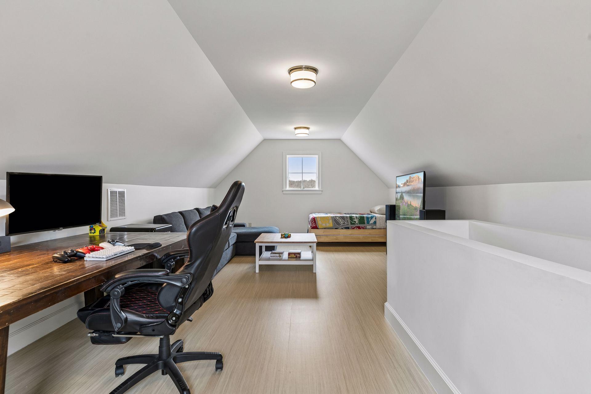 Versatile third floor amusement room with hardwood flooring, abundant natural light from two windows, and overhead lighting. Desk stays