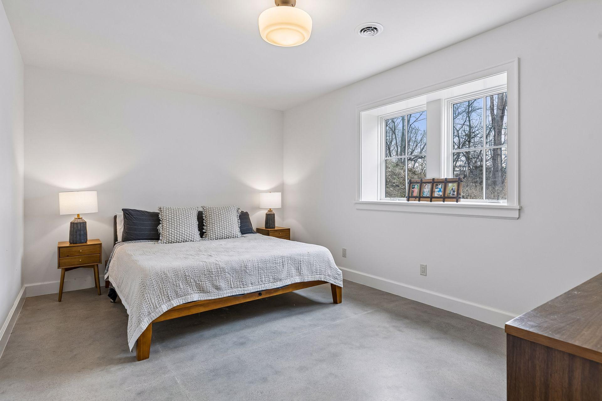 Spacious lower level bedroom with lookout windows, overhead light, and heated cement flooring, providing a flexible space to suit your needs.