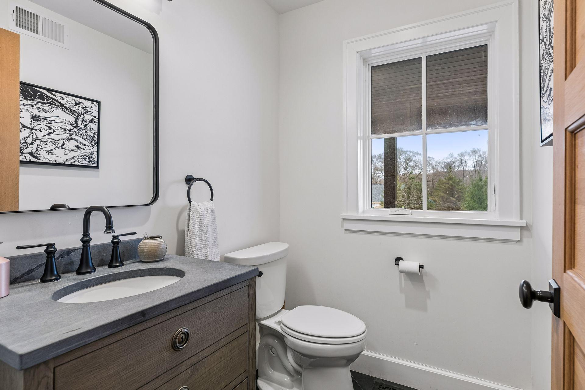 Main floor half bath featuring heated slate tile flooring, a stylish vanity with mirror, and a bright window.