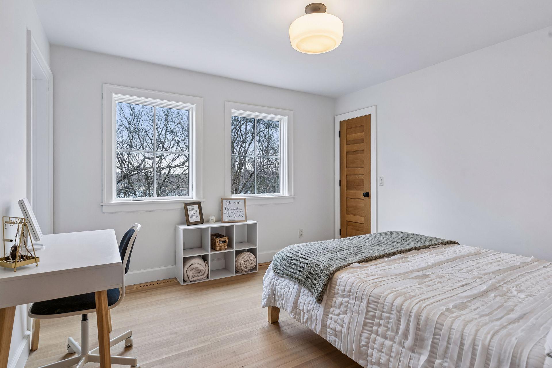 The second upper level bedroom, with hardwood flooring, ample natural light from two windows, overhead light, and a generous walk in closet.