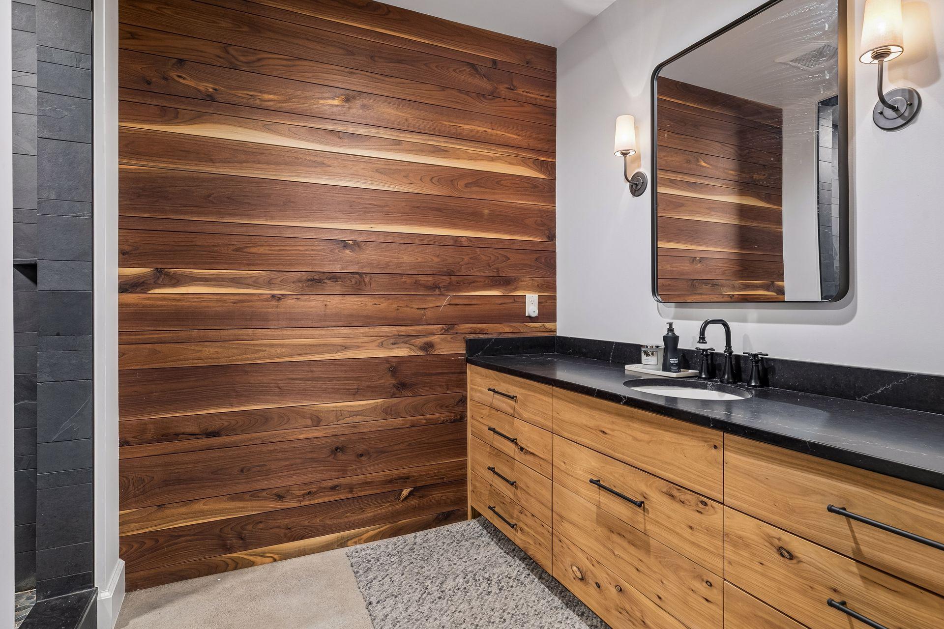 The lower level, 3/4 bath complete with heated cement flooring, a streamlined vanity sink, mirror, and stylish wall lighting. Black walnut accent wall with wood harvested from the property!