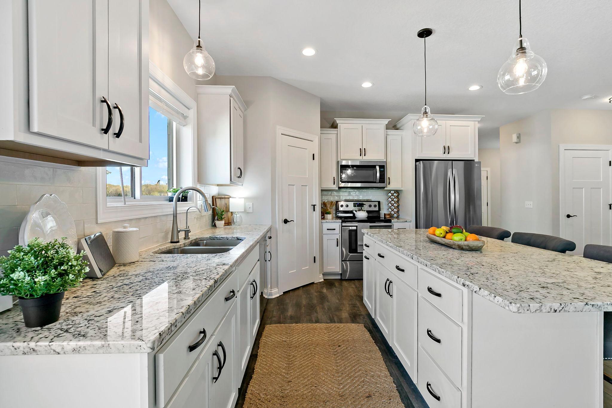 Elegant kitchen with expansive granite countertops, white cabinetry, and modern lighting.