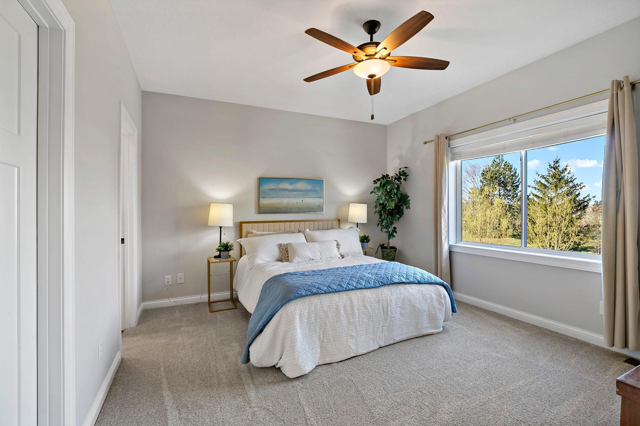 Bright and airy bedroom with large window, plush carpeting, and ceiling fan for added comfort.