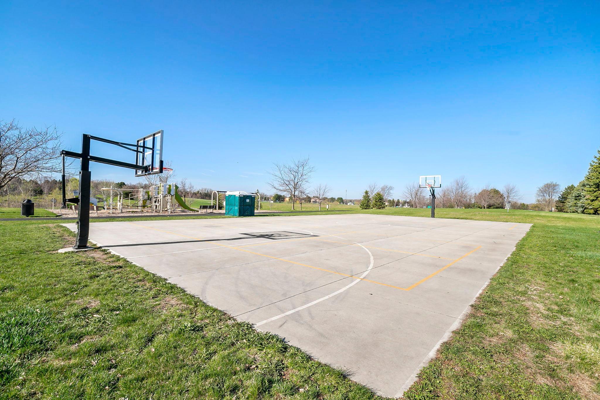 An outdoor basketball court beside a playground on a bright, clear day.