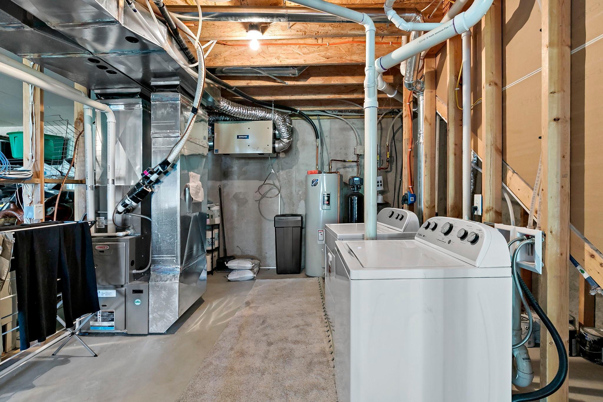 Unfinished utility room featuring laundry area, furnace, water heater, and ample storage space.