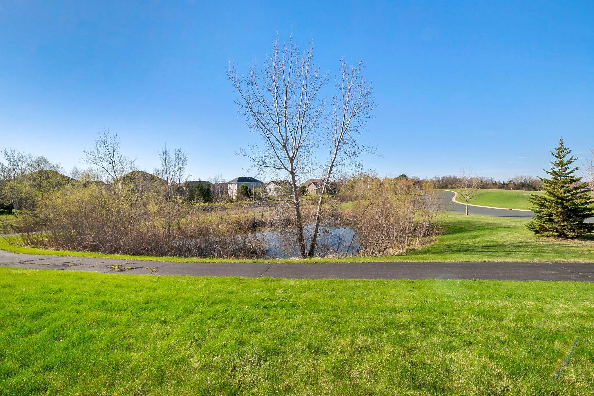 A peaceful neighborhood pond bordered by walking paths, grassy lawns, and nearby homes.