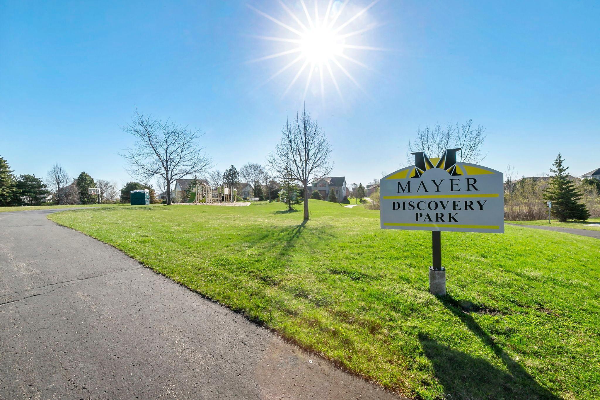 Sunny afternoon at Mayer Discovery Park, with open green space and a neighborhood playground in view.