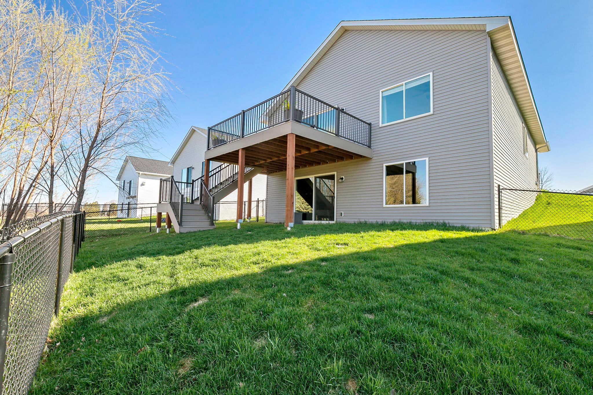 Backyard view of a modern home featuring an elevated deck, staircase access, and a spacious fenced lawn.