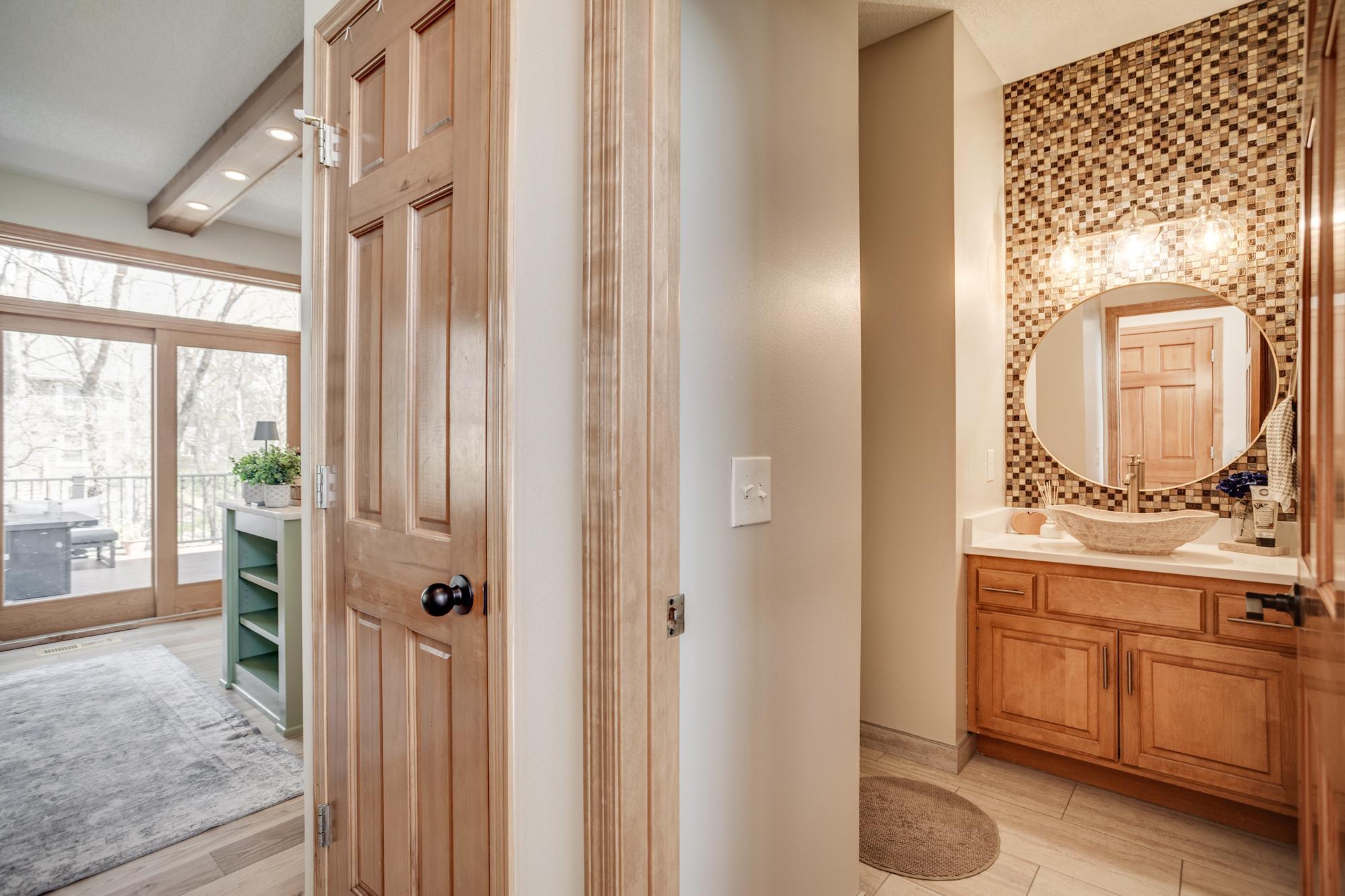 Perfect for guests, this stylish, updated powder bath makes a striking impression with its vessel sink, complemented by a mosaic tile accent wall, new lighting and sleek round mirror.