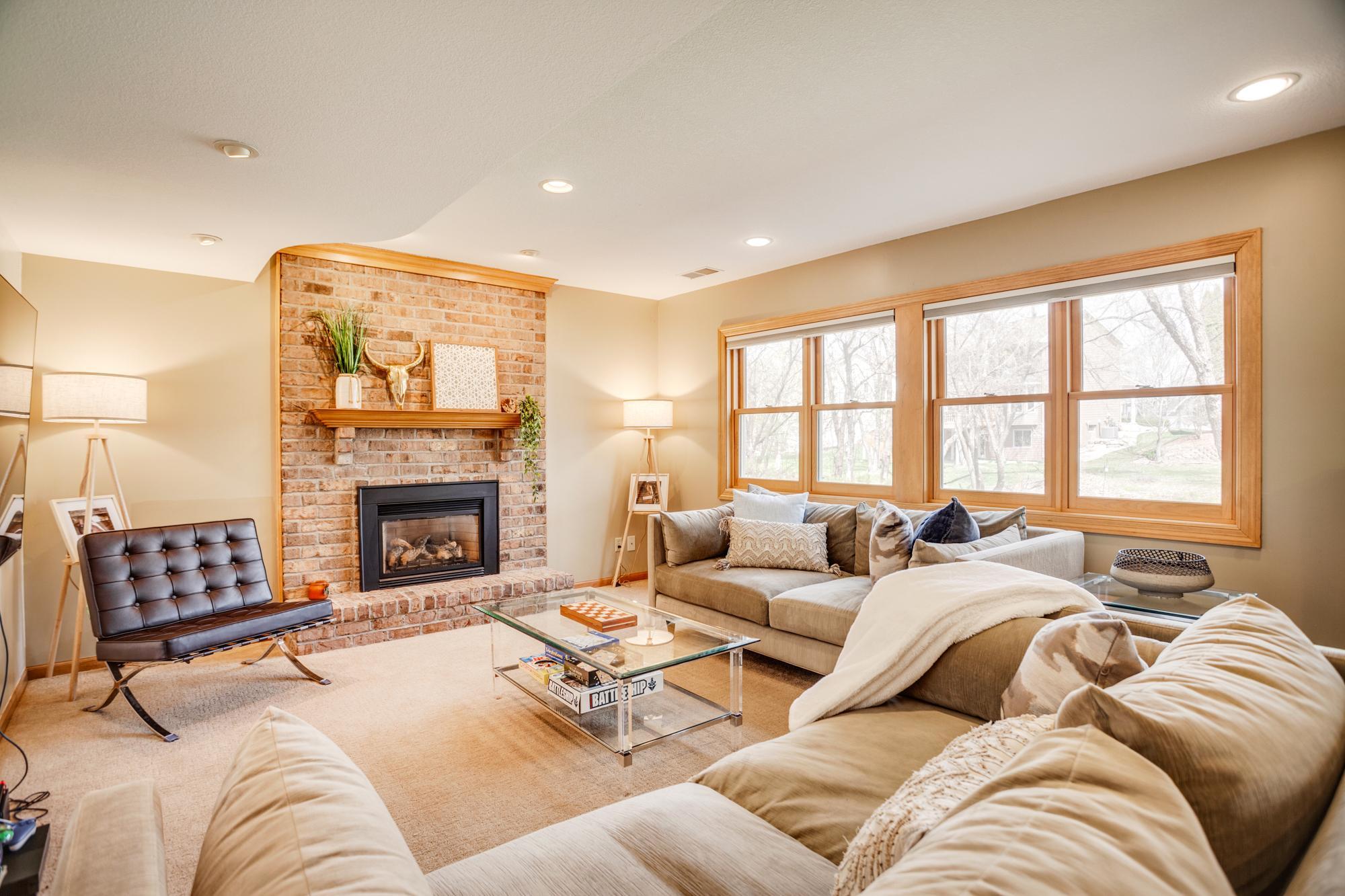 Showcasing a focal gas fireplace with floor-to-ceiling brick surround, the space features generous seating areas and large windows that bring in natural light and views of the backyard.