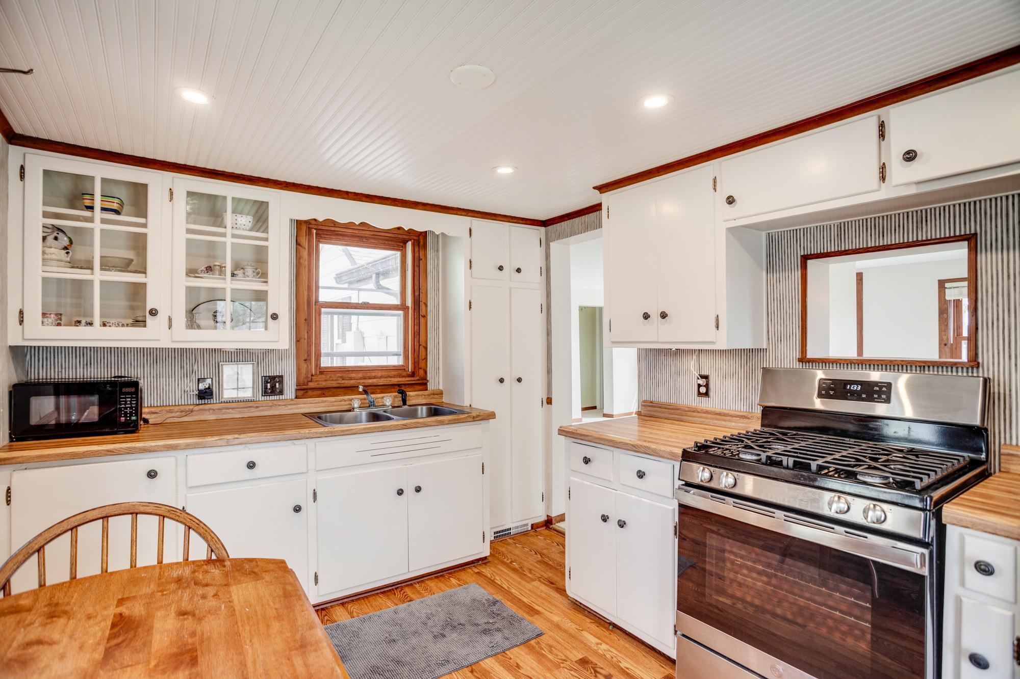 Even the kitchen is utterly charming with its hard flooring, beadboard ceiling, and enameled cabinetry with glass displays.