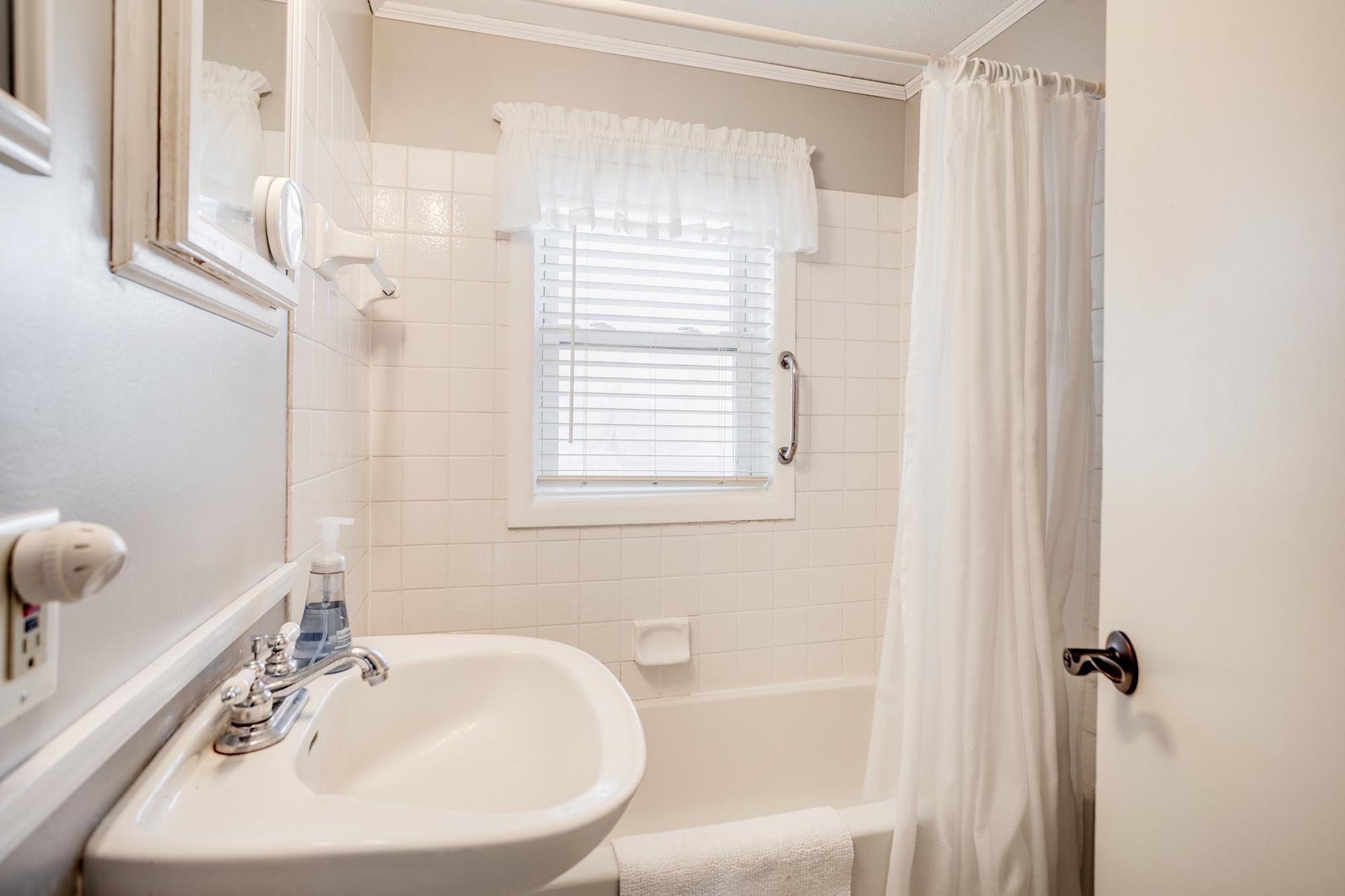 The full bath includes a pedestal sink, tile flooring and tile shower/tub surround.