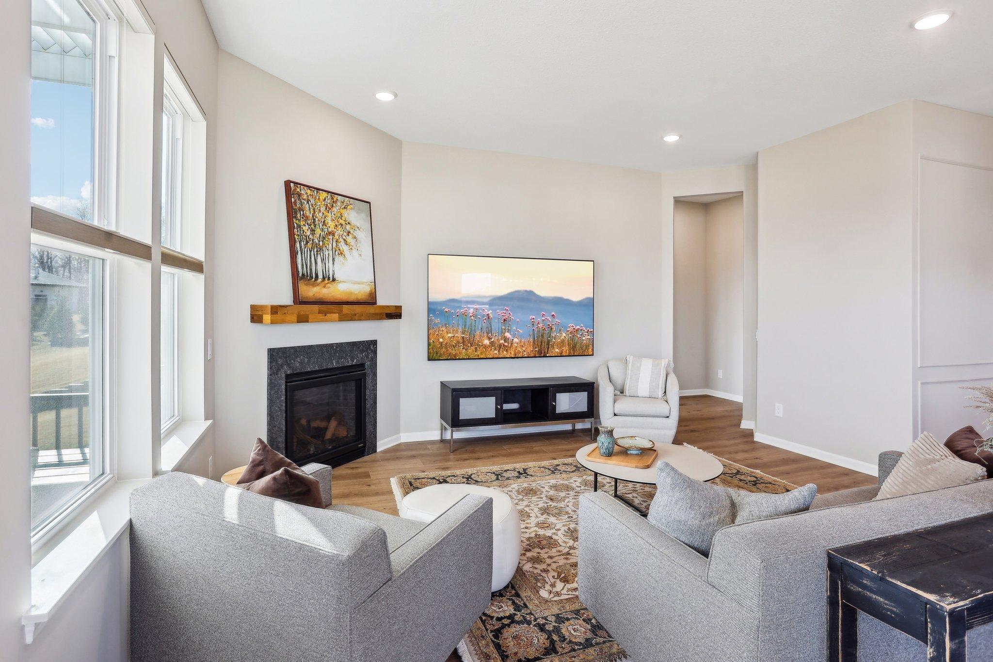 Bright and inviting living room featuring large windows that fill the space with natural light, a cozy fireplace with a stylish wood mantel, and an open-concept layout perfect for relaxation and entertaining.