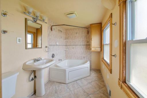 Upper-level primary bath featuring a full tub, natural light, and a functional layout