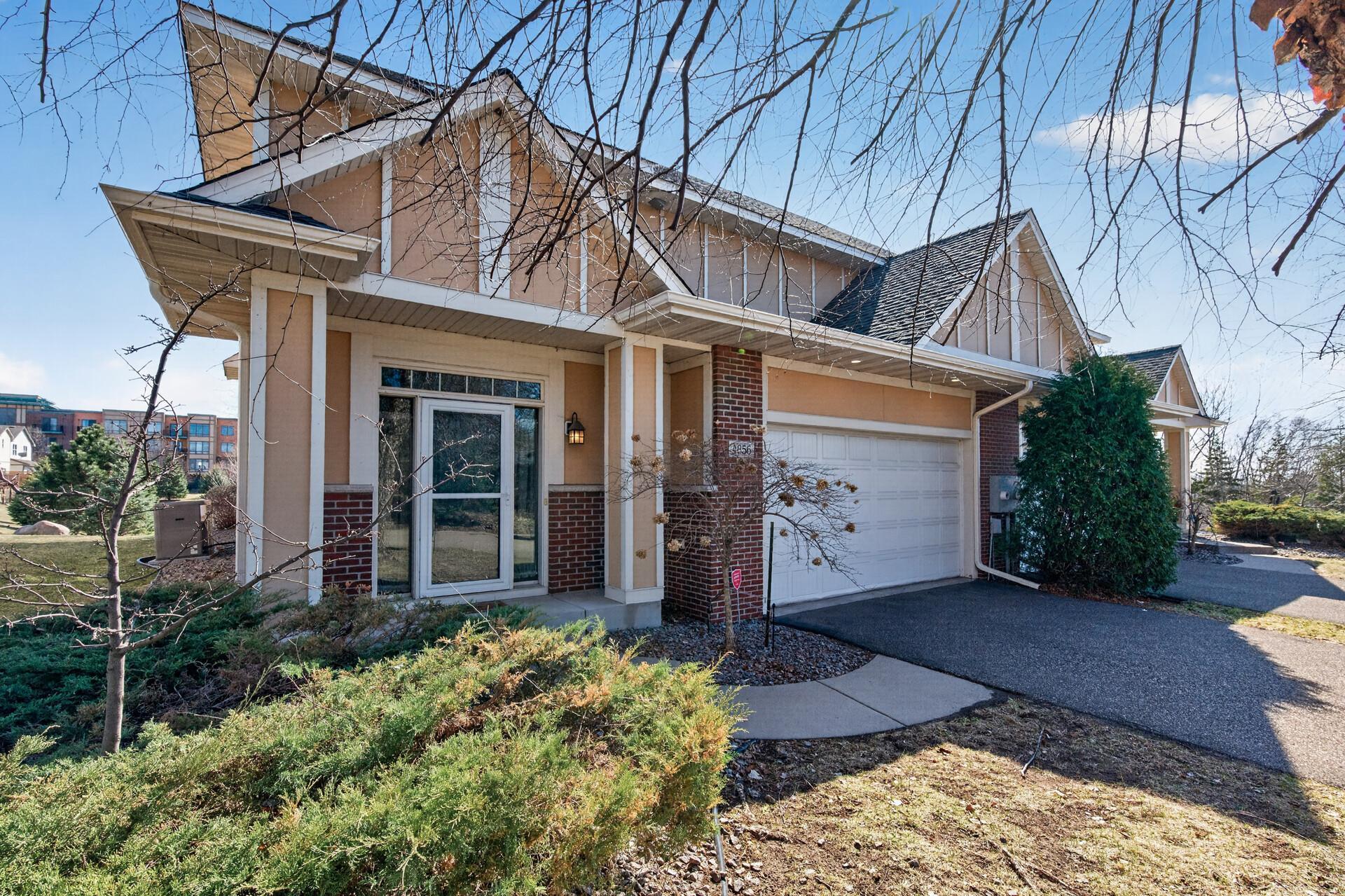 Side view of the front exterior showcasing charming curb appeal with a covered entry, mature landscaping, and an attached 2-car garage. The well-maintained façade blends brick and siding for timeless appeal.