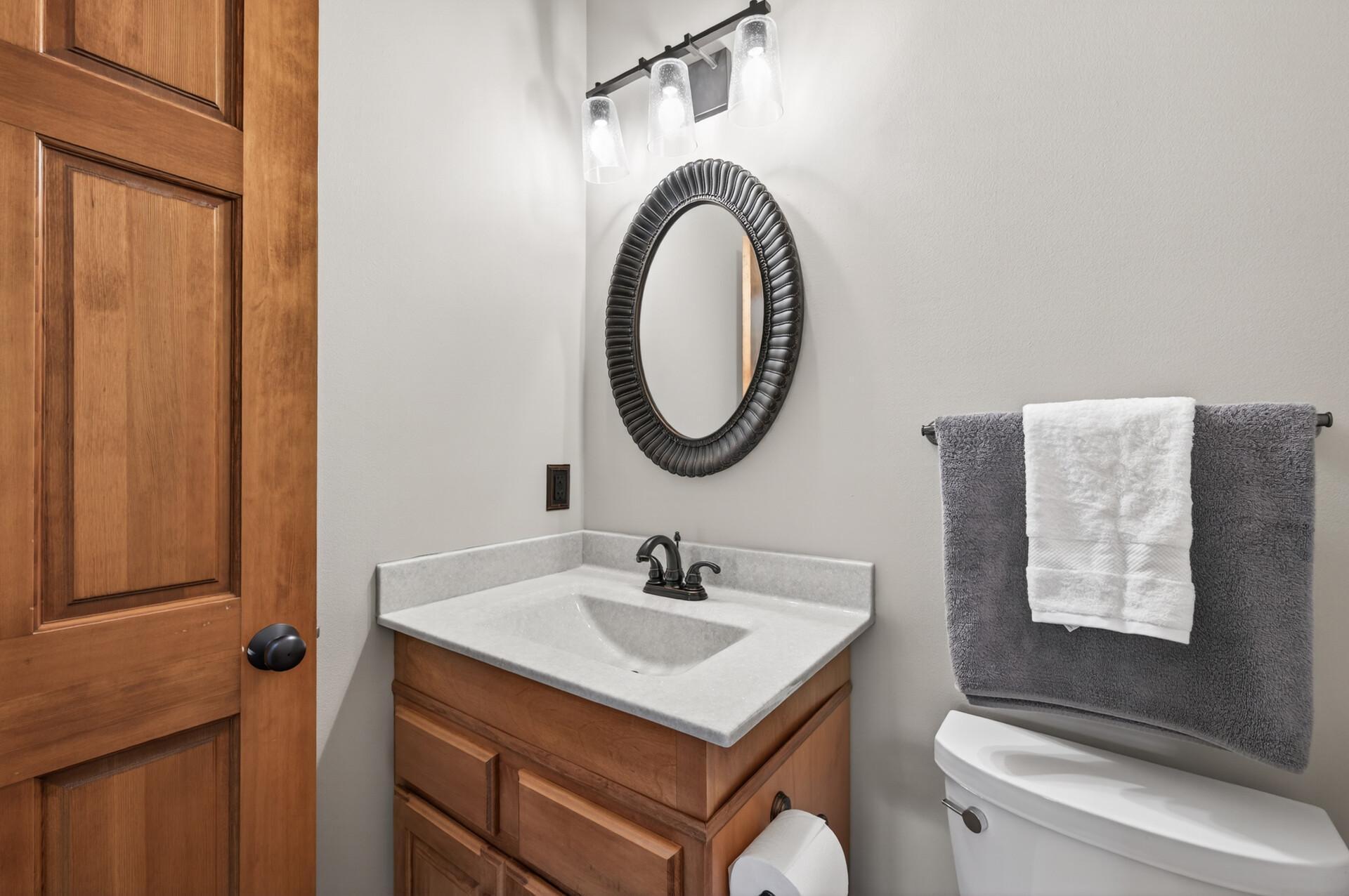 Stylish main-level half bath featuring a solid surface vanity, modern lighting, and warm wood cabinetry. Clean finishes and a neutral palette create a polished, functional space.