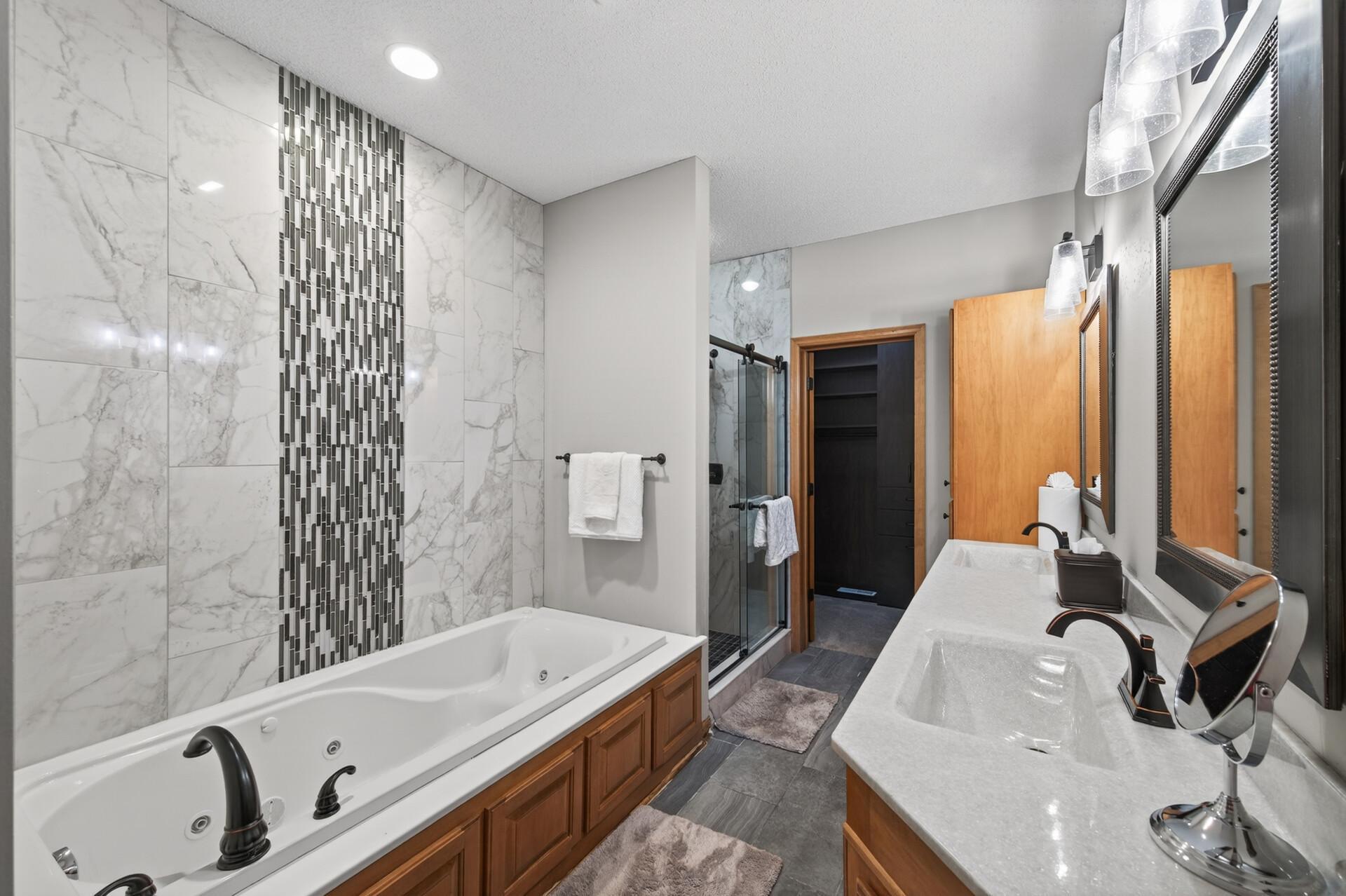 Luxurious en-suite bathroom featuring a jetted soaking tub, dual vanity, and a walk-in tiled shower. Elegant tilework and updated fixtures create a spa-like experience.