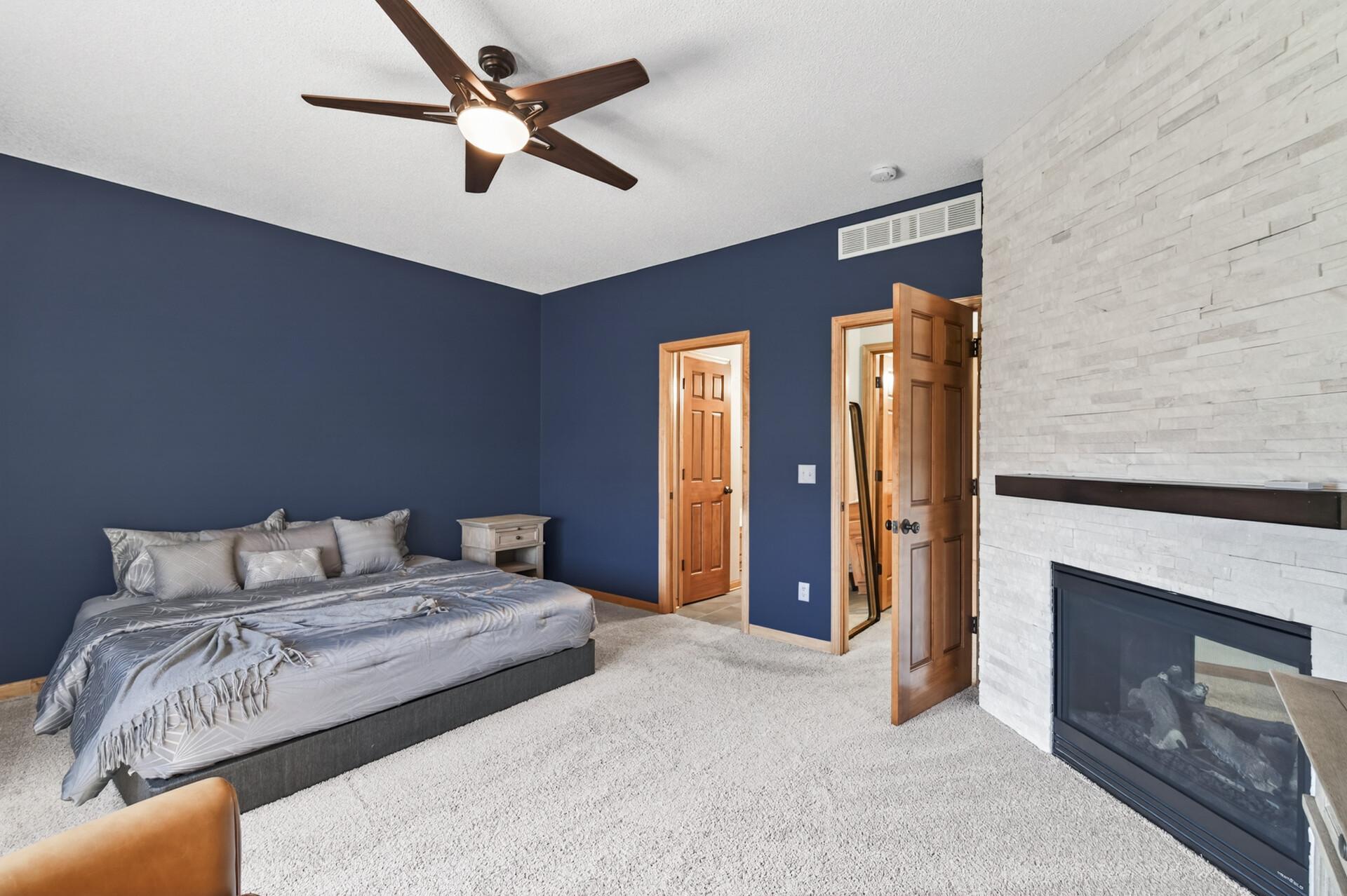 Beautiful stone-accent fireplace adds warmth and character to the primary bedroom. Large windows enhance natural light while maintaining a peaceful, inviting atmosphere.