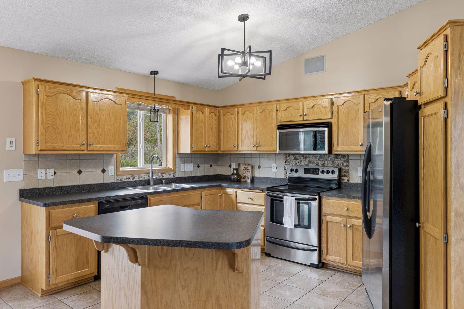 Well-designed kitchen with ample cabinet and counter space, decorative backsplash accents, updated lighting, and a center island ideal for meal prep or casual seating.