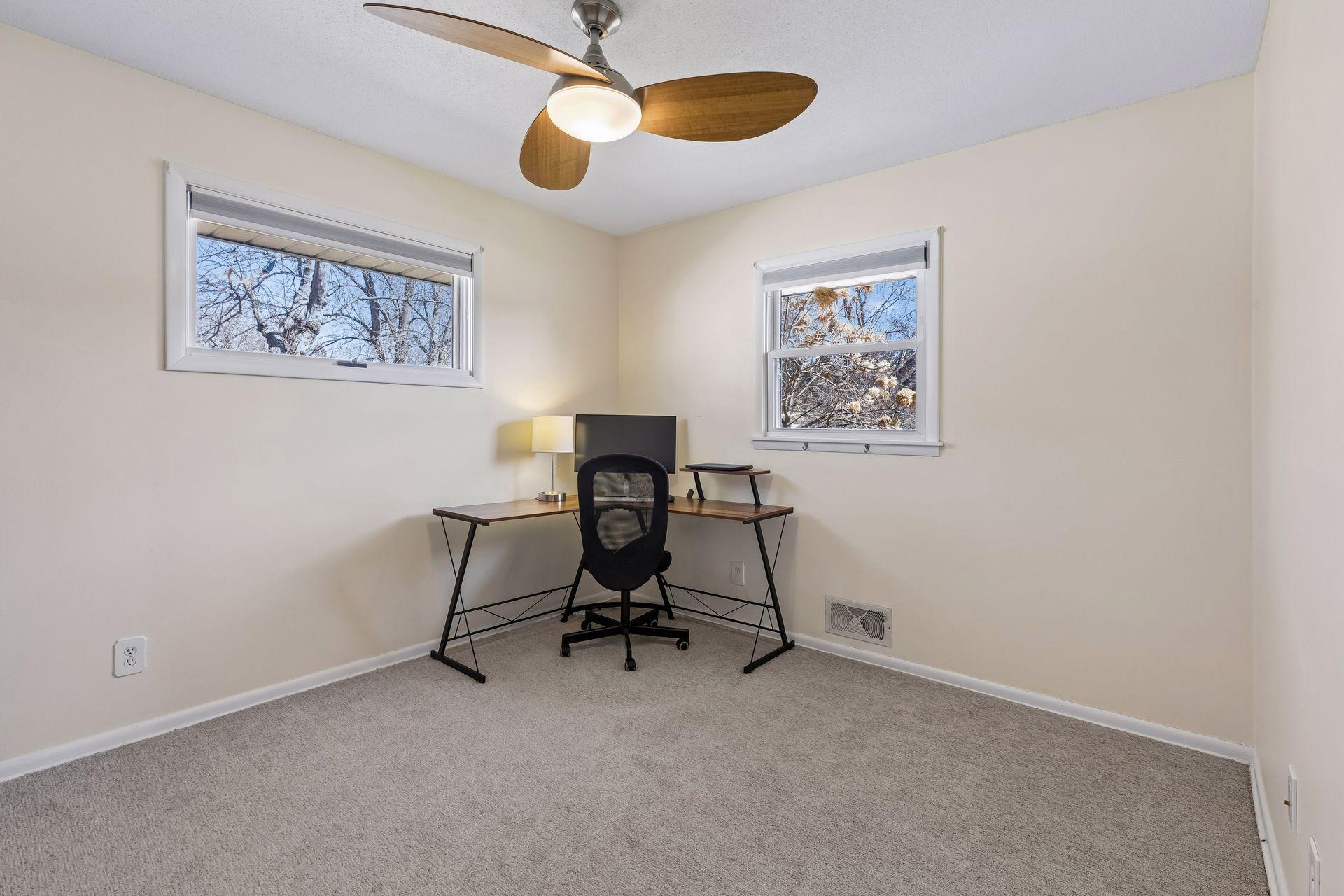 Versatile bedroom or office space with dual windows, ceiling fan, and great natural light.