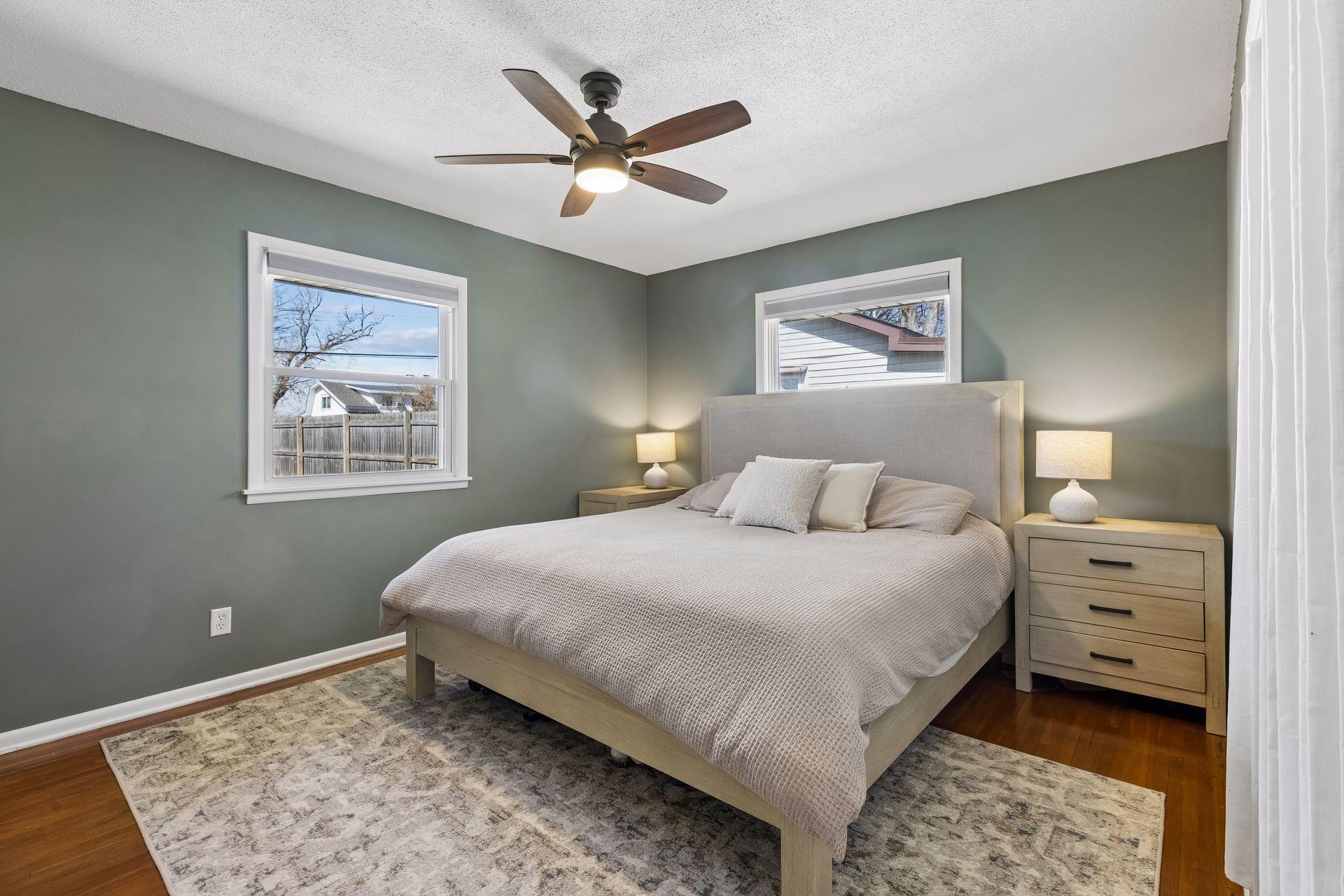 Inviting bedroom featuring hardwood floors, two windows for great natural light, and a ceiling fan for added comfort.