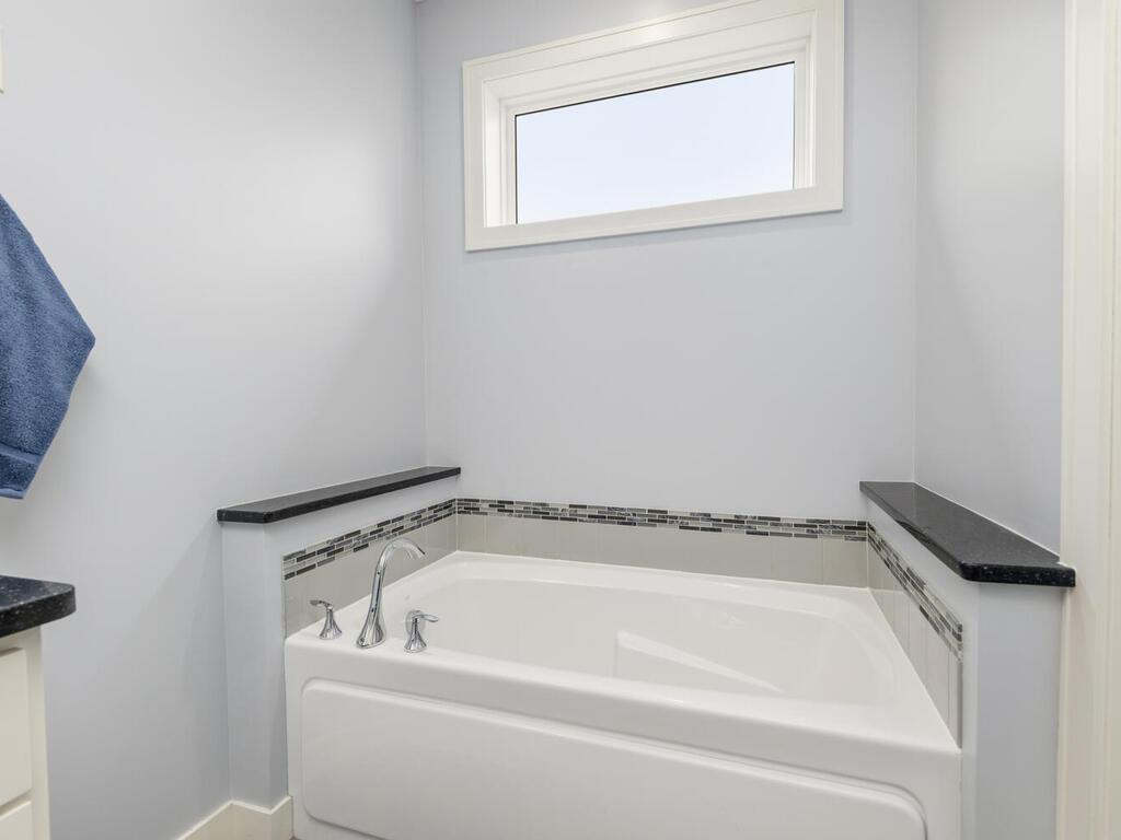 Soaking tub with tile surround and natural light from transom window.