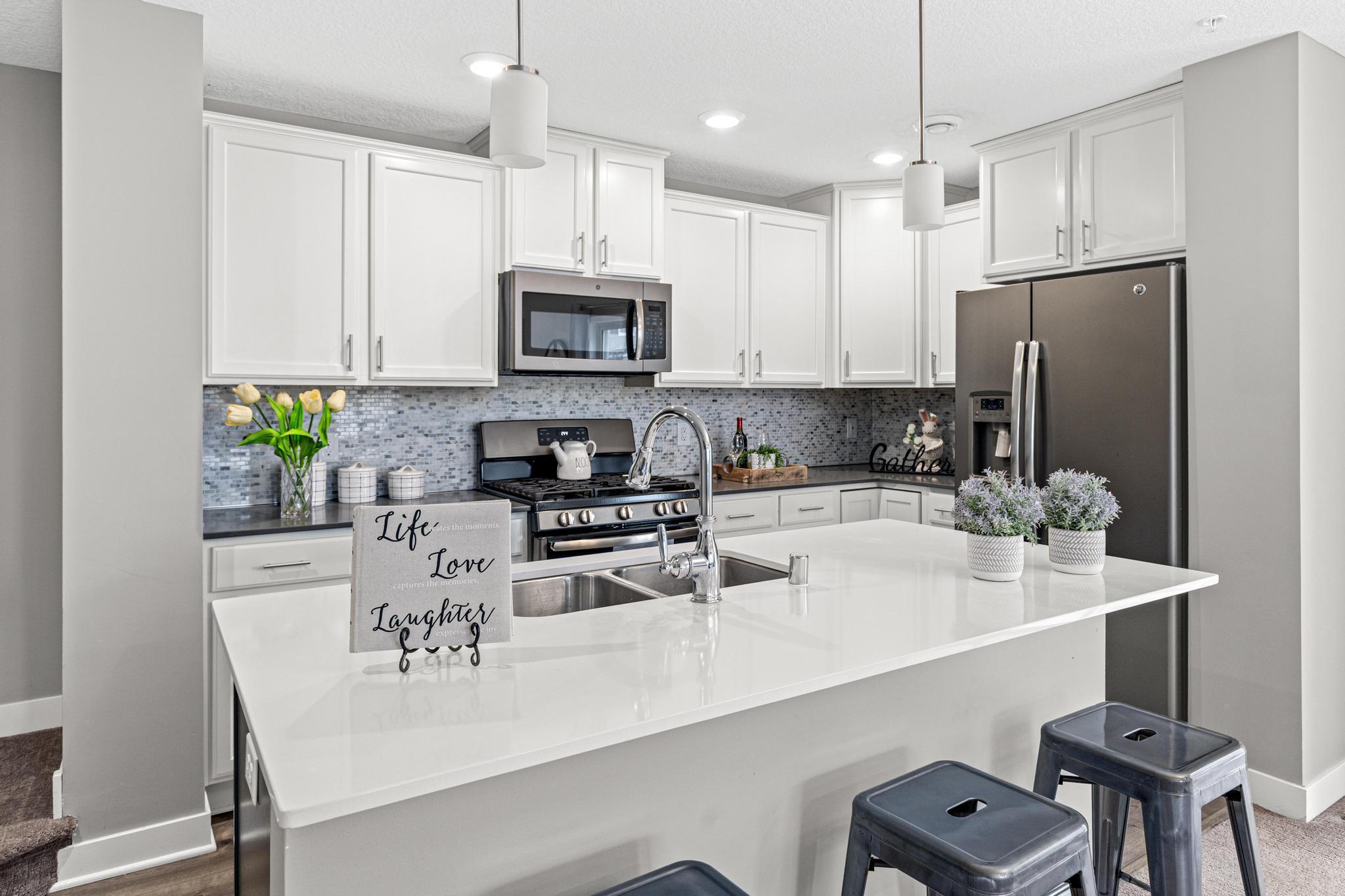 A close-up of the kitchen’s finishes, featuring sleek quartz countertops, a contemporary tile backsplash, and a suite of stainless steel appliances including a microwave, oven, and refrigerator.