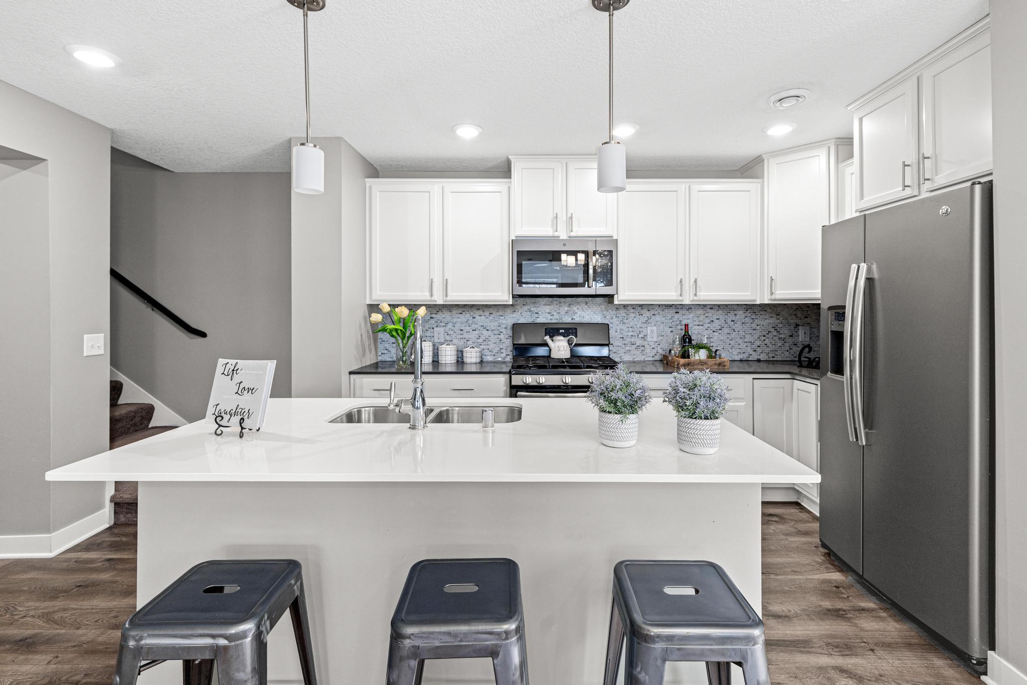 A detailed look at the expansive quartz island and stainless steel appliances. This central location provides easy access to the living areas and the staircase leading to the upper-level bedrooms.