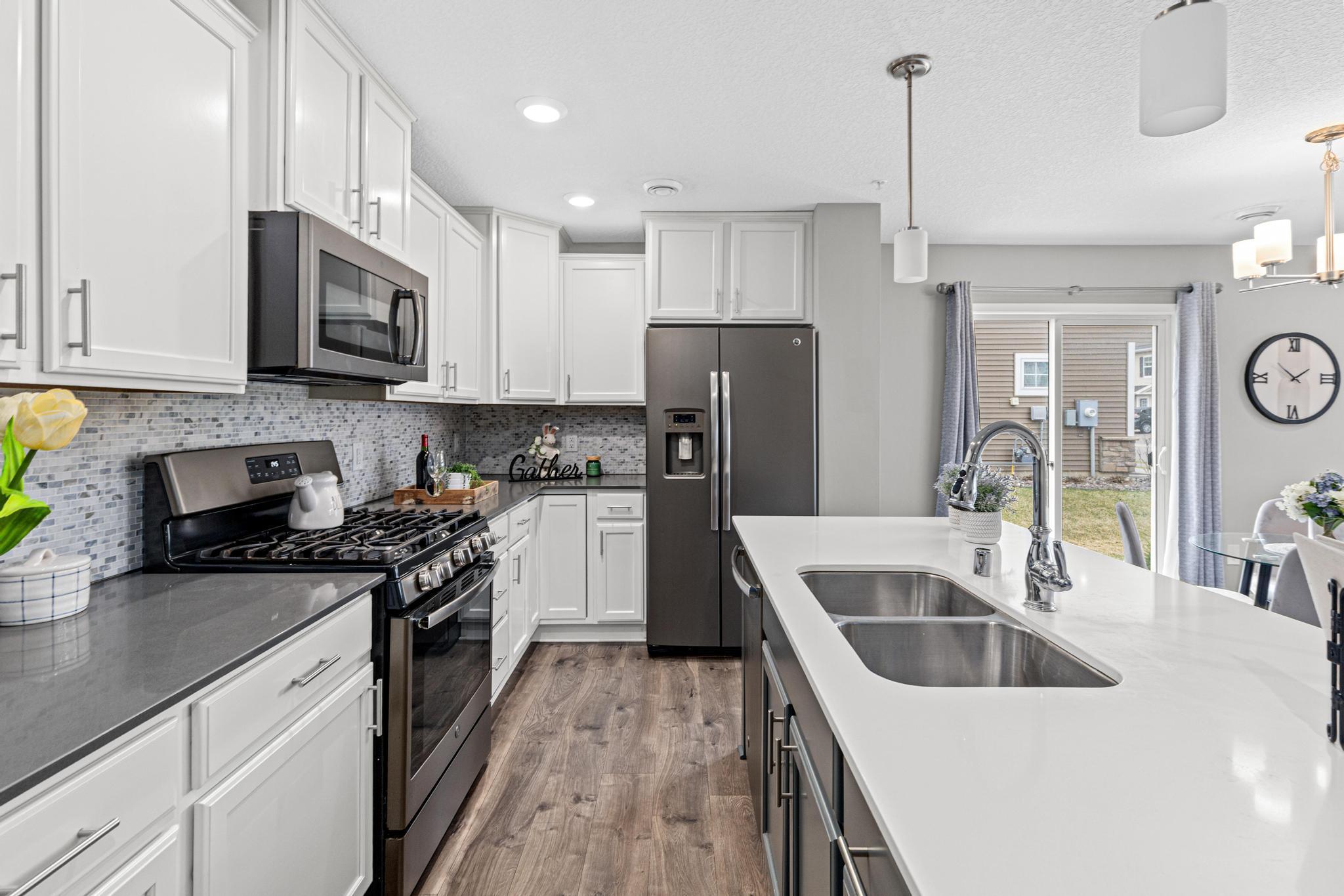 Highlighting the custom-feel cabinetry with soft-close hinges and a convenient tuck-under garbage and recycling center. Paired with stainless steel appliances and a modern backsplash, this kitchen is as functional as it is stylish.