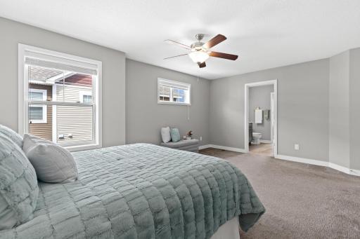 Spacious primary suite with a view toward the ensuite and walk-in closet. Two windows provide beautiful natural light, while the ceiling fan adds comfort to this serene retreat, seamlessly connecting the sleeping area to the private bath.