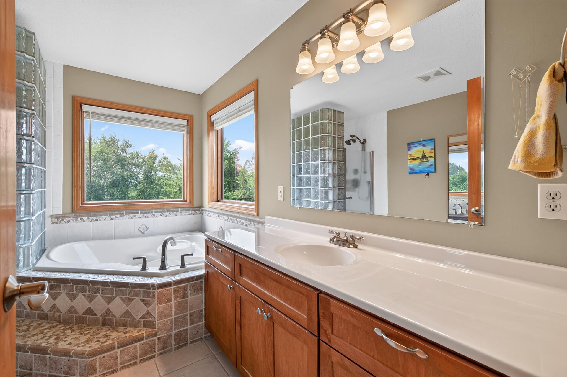 bathroom suite with dual sinks, corner jetted tub and a corner glass blocked walk in shower.