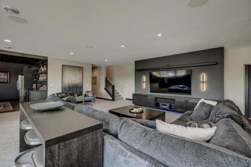 The walkout lower level offers a sprawling family room, a stunning full-service bar with a floor-to-ceiling tiled accent wall, stainless steel refrigerator, microwave, dishwasher, and sink.