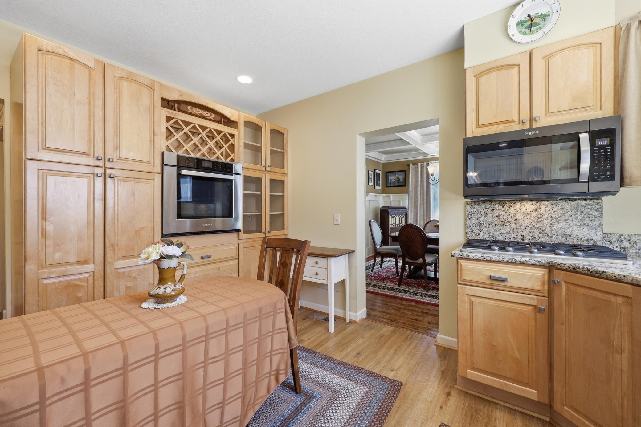 Kitchen with maple cabinetry, built-in oven, microwave, granite countertops, gas cooktop, display cabinet, and storage cabinets.