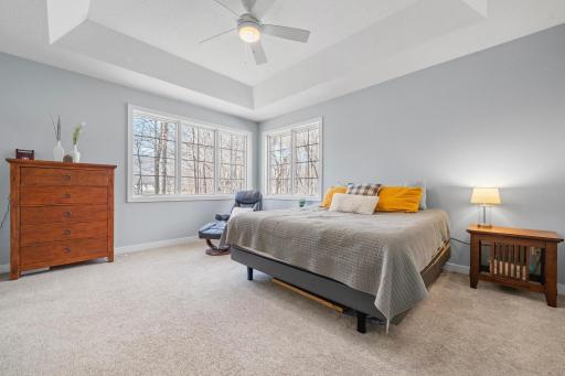 The primary bedroom offers a serene retreat with calming tones, abundant natural light, a vaulted tray ceiling, and a ceiling fan for added comfort.