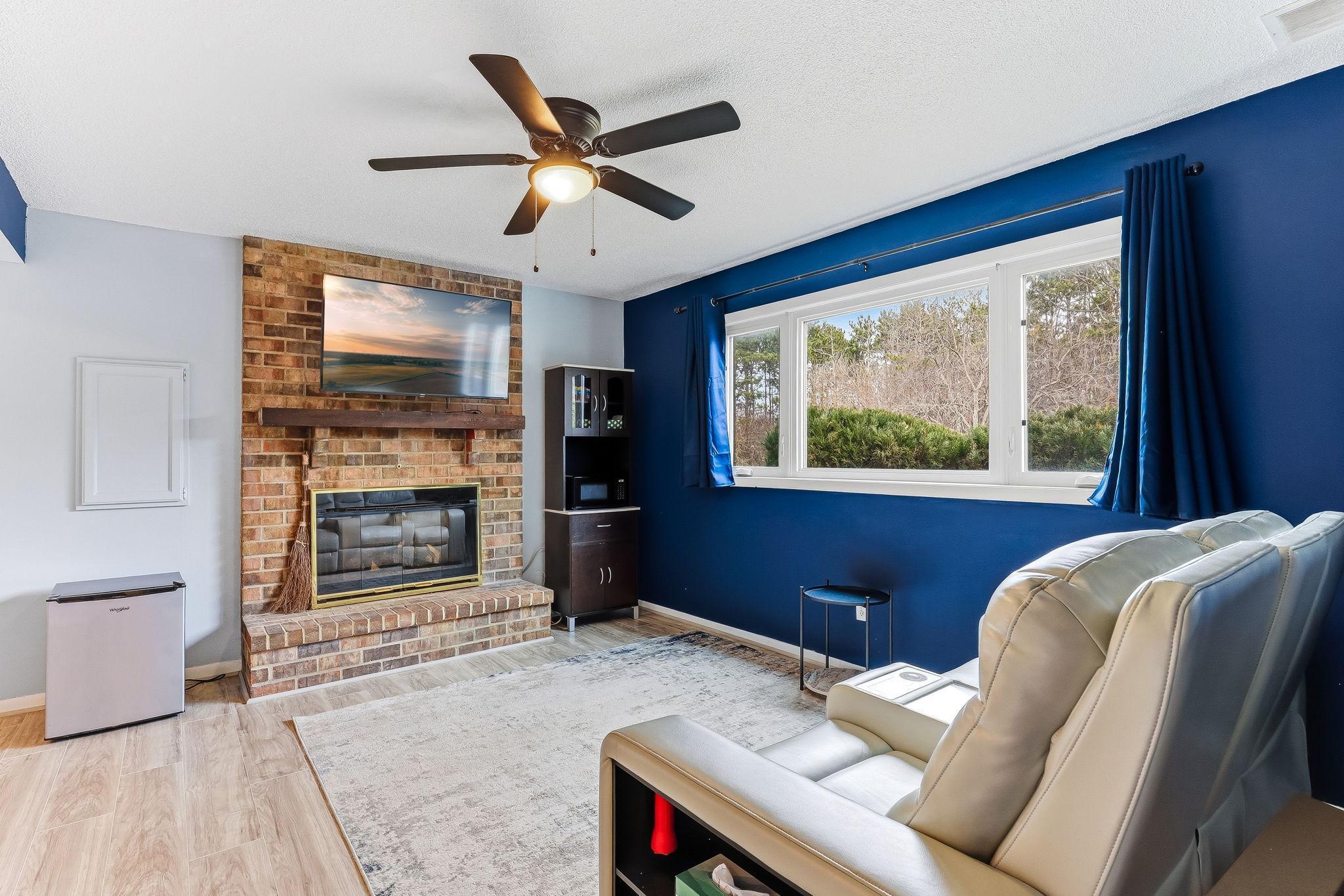 Lower-level living space with brick fireplace, large window, and natural light, creating a comfortable secondary gathering area.