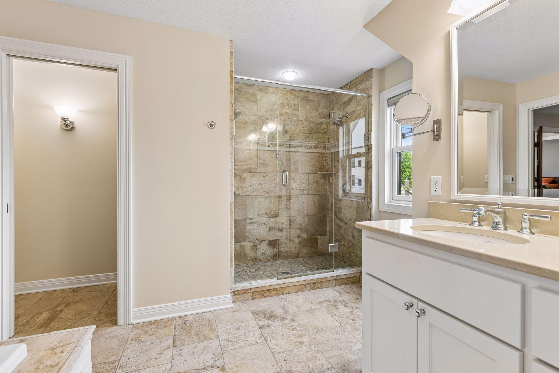 Spa-inspired primary bath featuring a whirlpool soaking tub, ceramic tiled shower, dual sinks, and a two-sided fireplace for the ultimate private retreat.