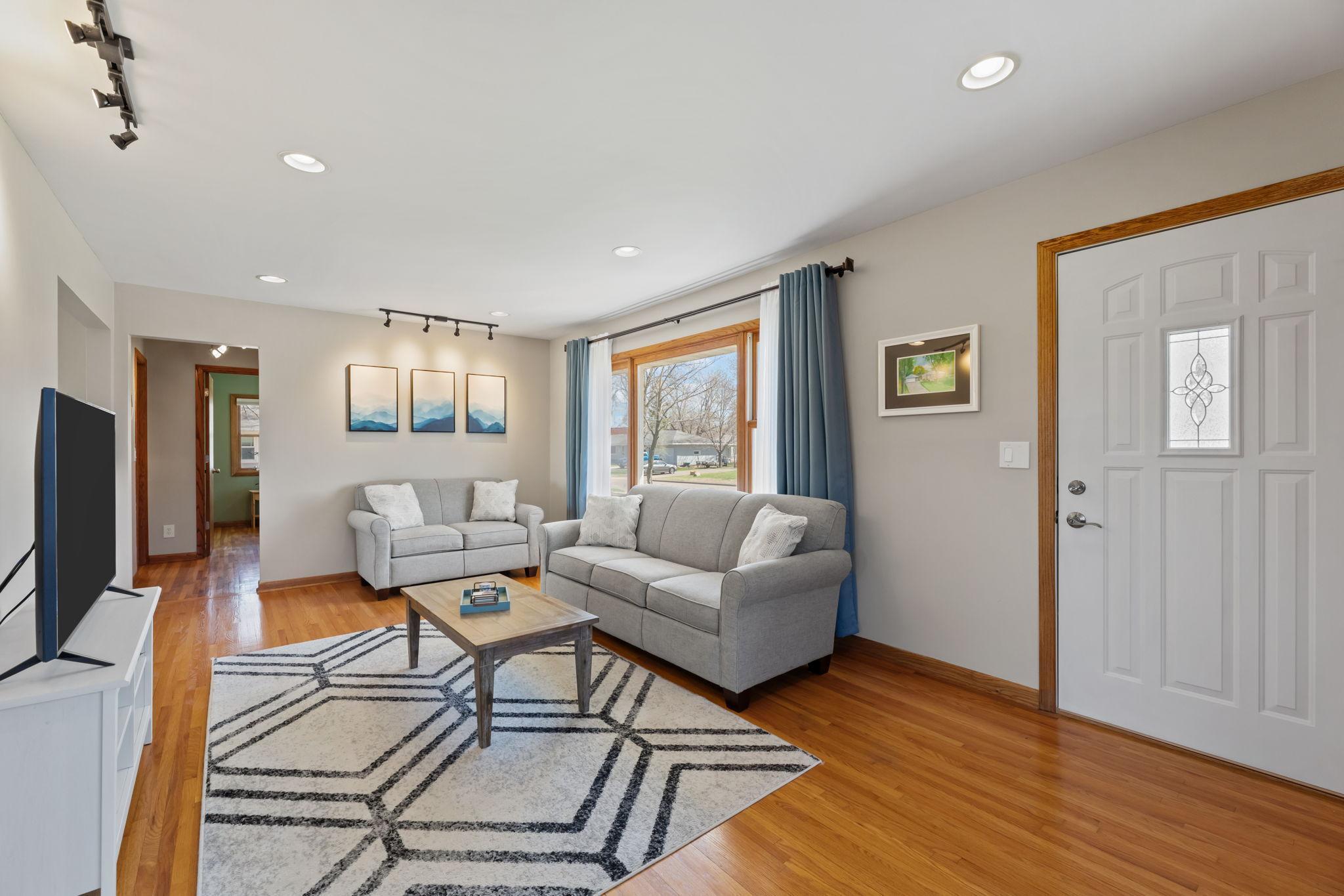The main-level living room showcases abundant natural light, beautiful hardwood floors, and track lighting, creating a warm and inviting space for entertaining.