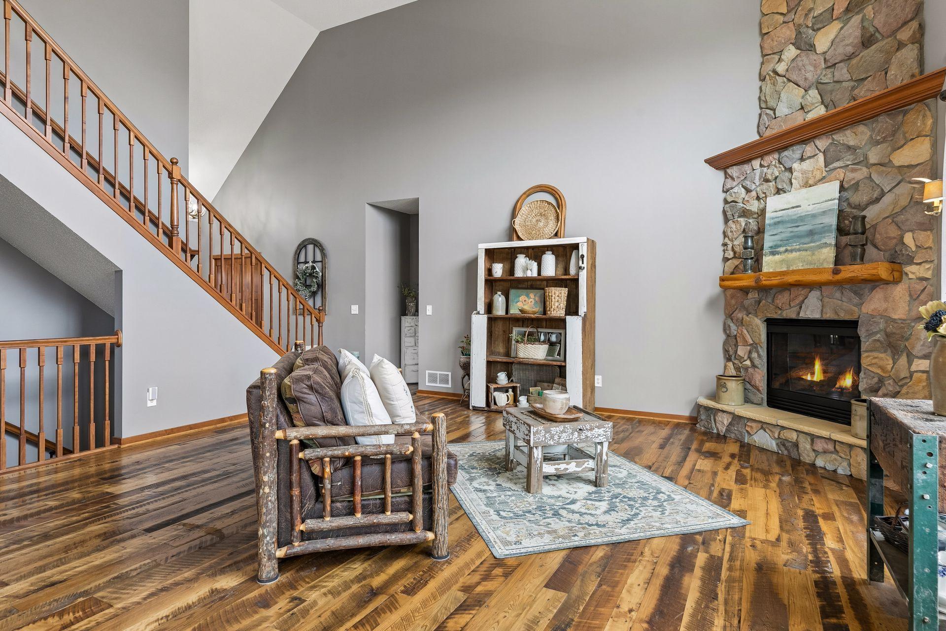 Great Room with two-story vault, reclaimed hardwood floors, and floor-to-ceiling stone gas fireplace.