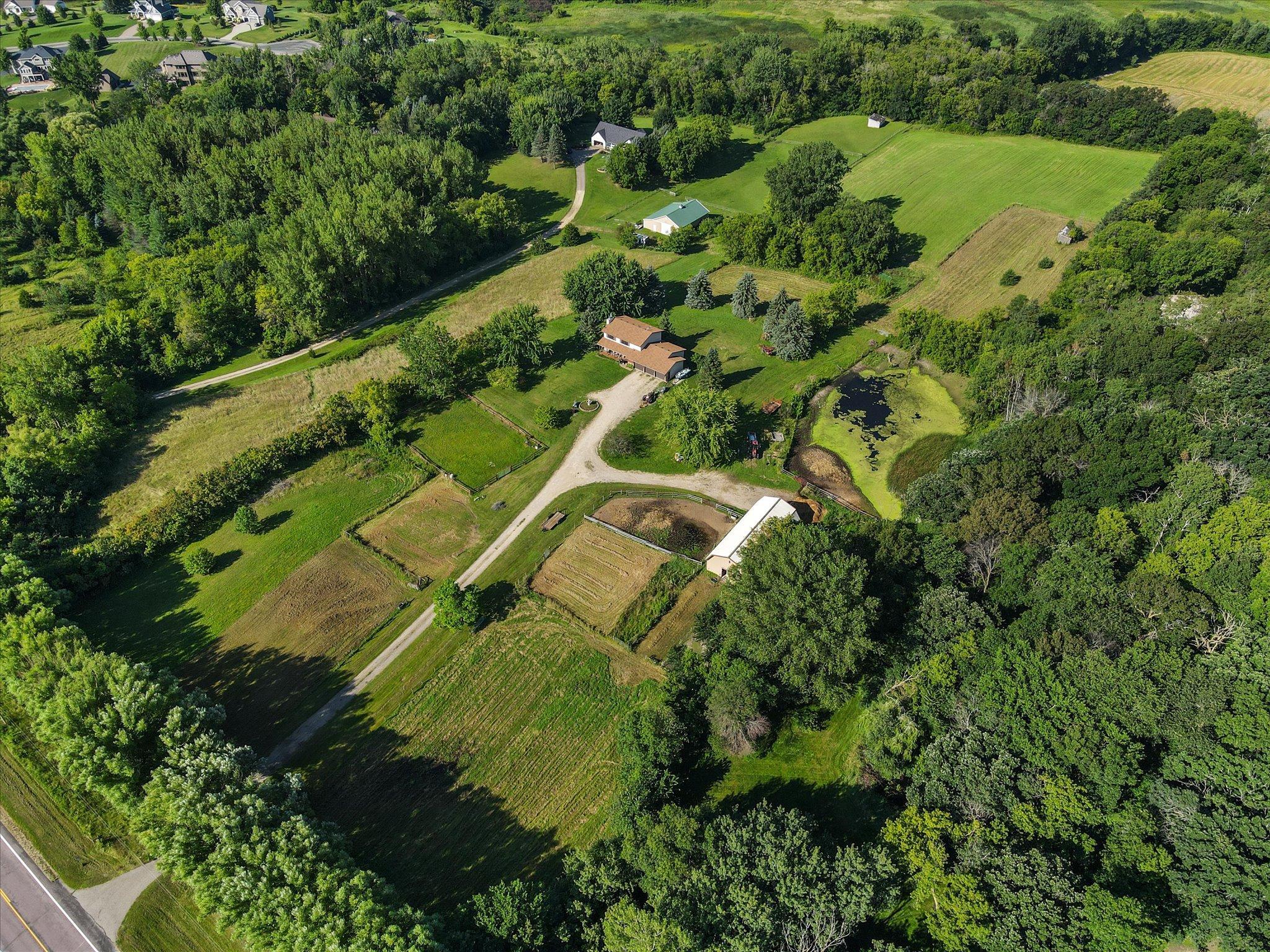 Incredible aerial perspective showcasing the full property setting with mature trees, open acreage, hobby farm amenities, and peaceful privacy.