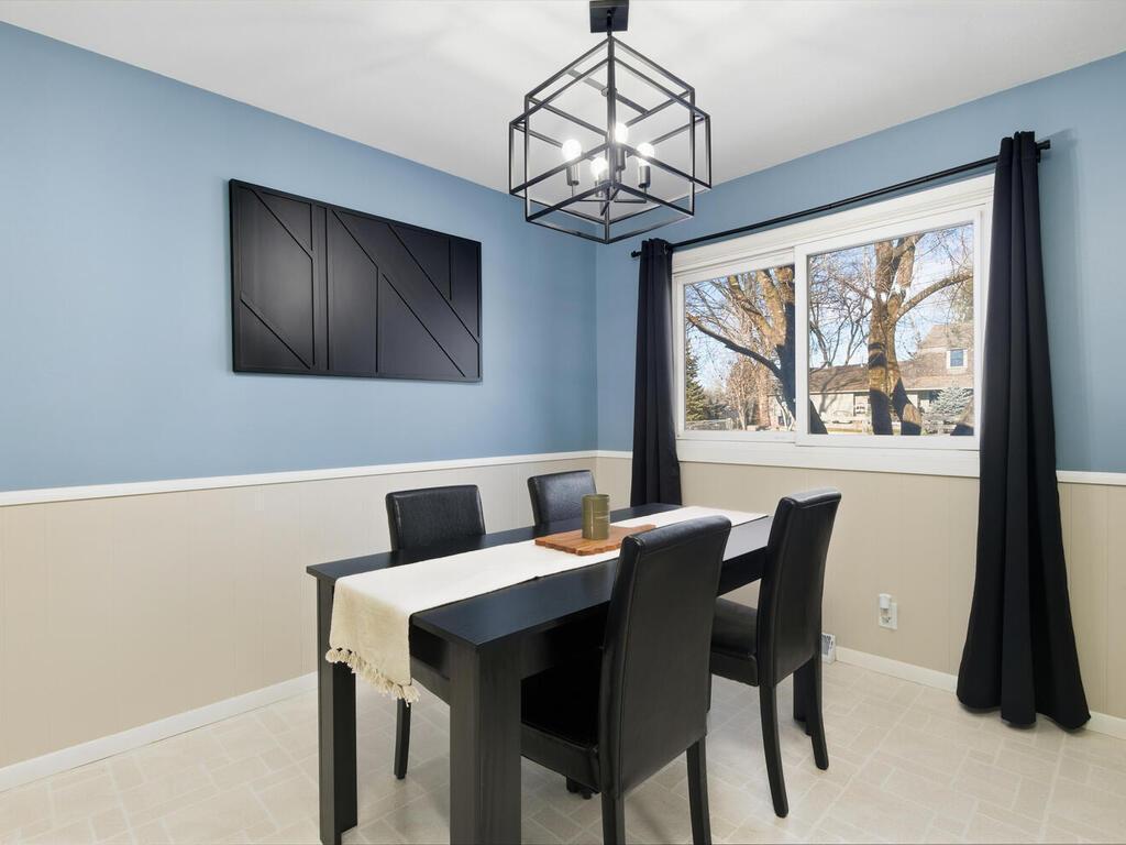 Enjoy meals in the stylish dining area, featuring a modern chandelier, updated wainscoting, and large windows overlooking the yard.