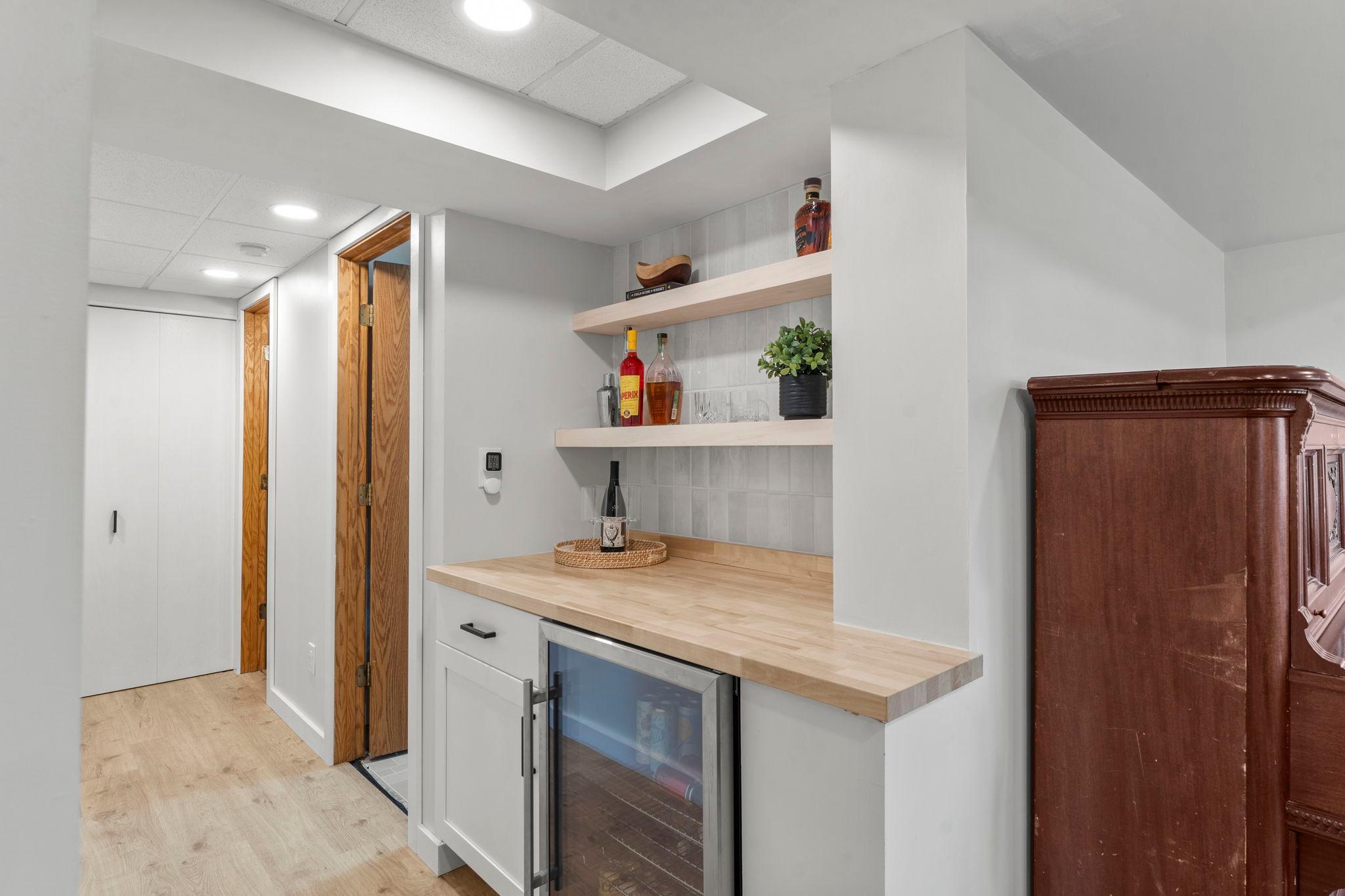 The recreation space connects to an updated bar area complete with a beverage fridge, countertop space, shelving, and tile backsplash—perfect for entertaining.