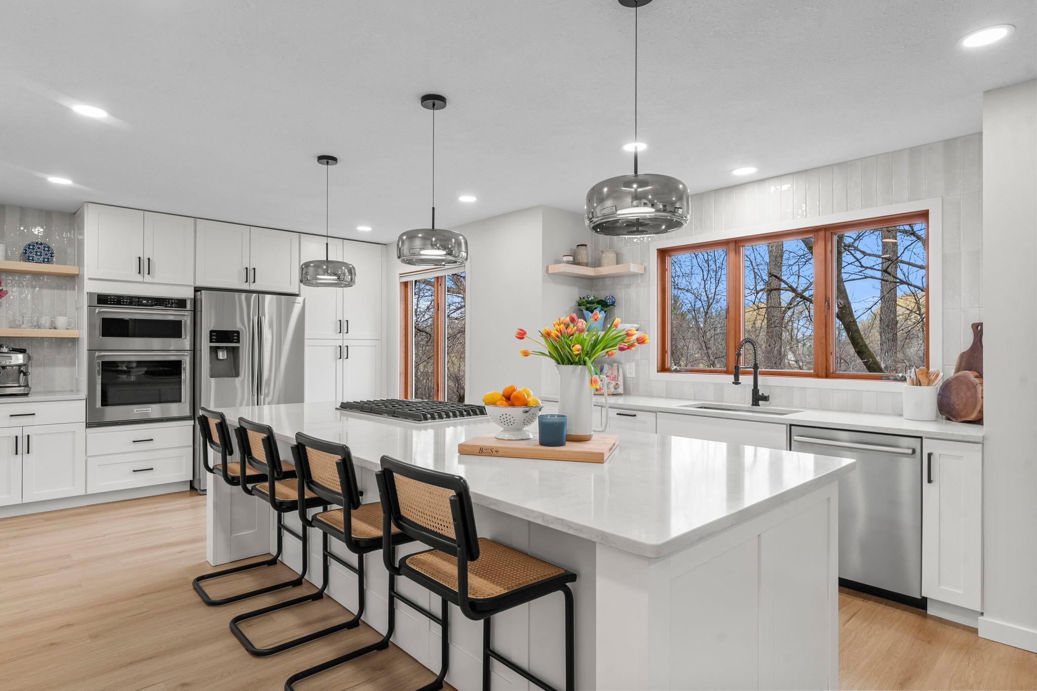 The fully remodeled kitchen (2024) is a true showpiece, featuring luxury plank flooring, crisp white cabinetry, expansive updated countertops, and a large center island with breakfast bar seating.