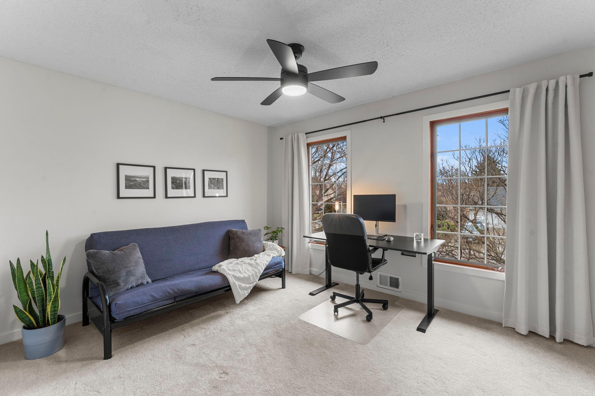 Bedroom four features carpeting, a ceiling fan, and large front-facing windows that fill the room with natural light.