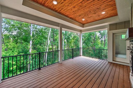 An inviting covered deck designed for entertaining, complete with a wood ceiling, see-through fireplace, and tranquil wooded backdrop.