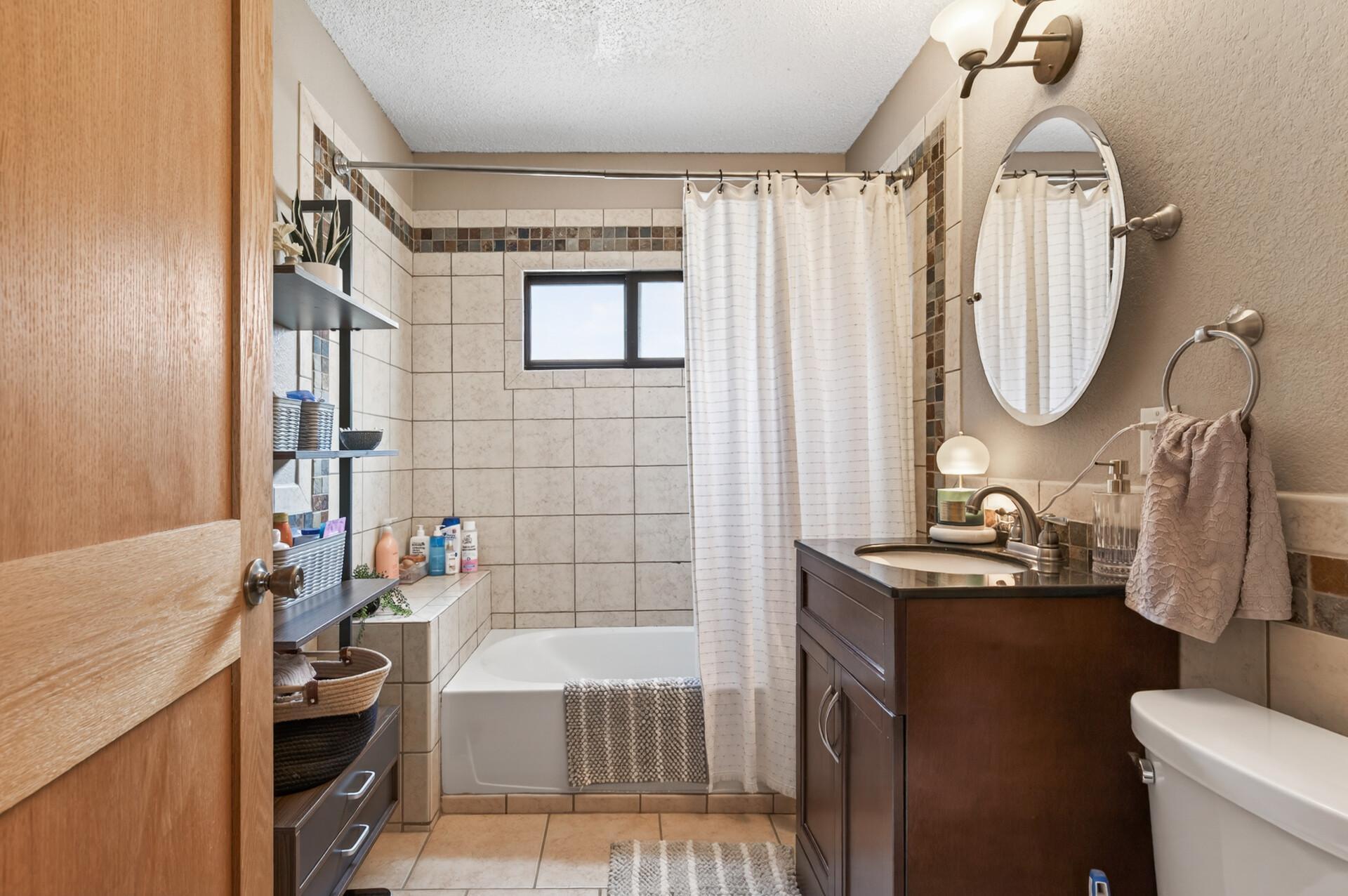 Full bathroom with tiled floors, tiled shower, and vanity with storage.